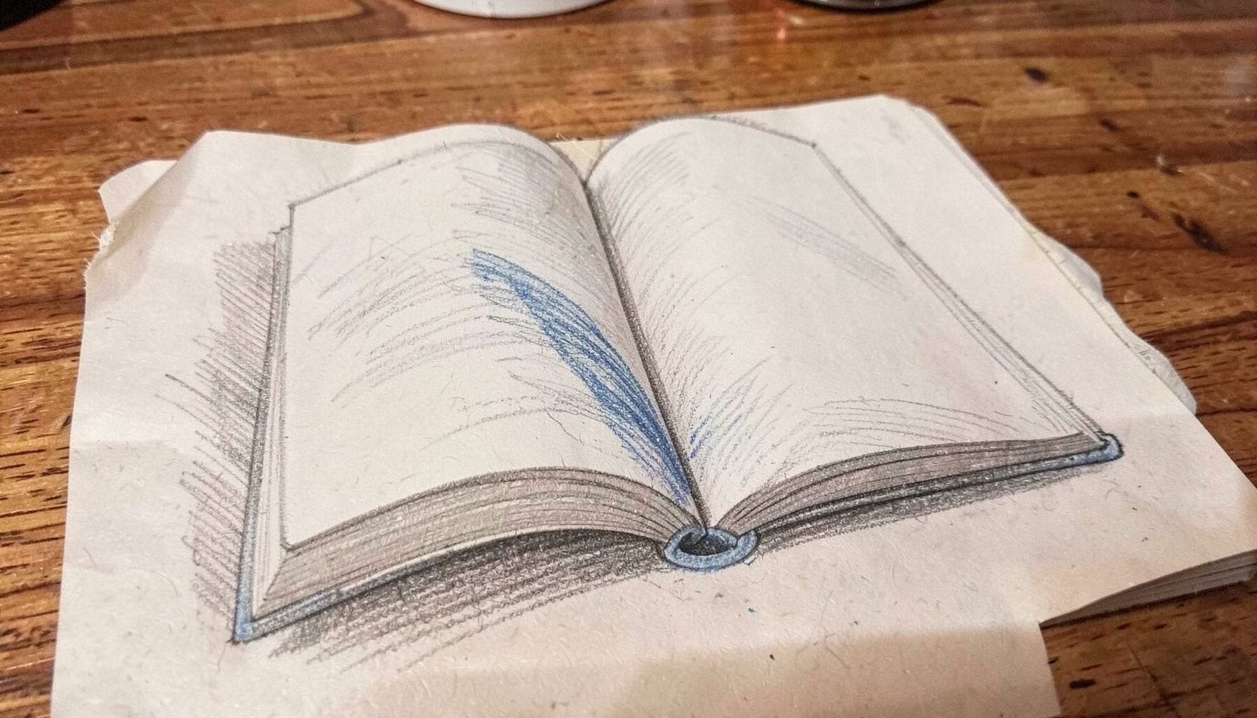 Graphite pencil sketch of an open book resting on a wooden desk, with soft cross-hatched shading in warm gray tones